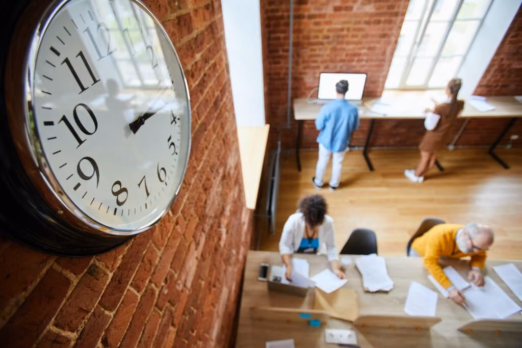 Équipe au travail dans un bureau, avec une grande horloge au premier plan
