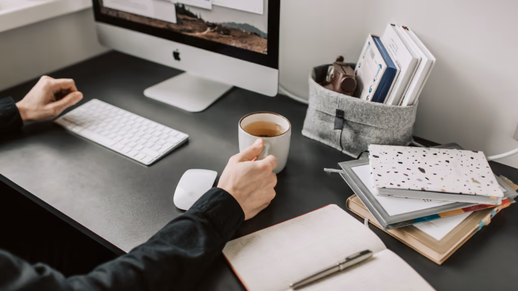 Bureau organisé avec ordinateur, carnet, livres et tasse de thé